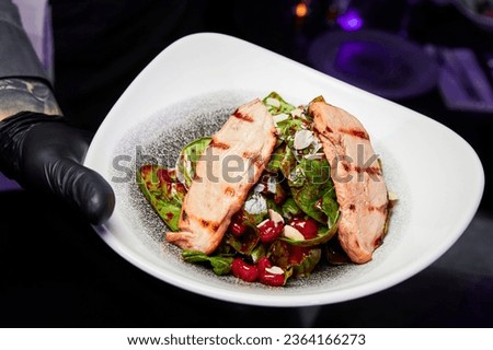 Waiter holding a platter with grilled veal pieces salad, vegetables and cherry sauce