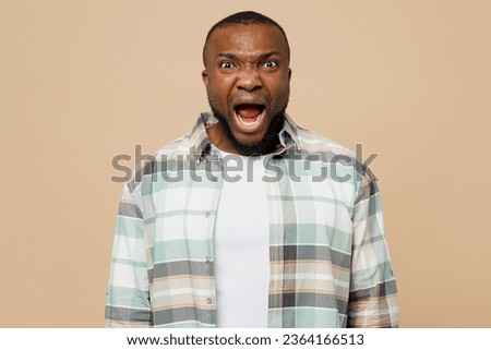 Young sad mad angry furious man of African American ethnicity wear light shirt casual clothes look camera scream shout cry isolated on plain pastel beige background studio portrait. Lifestyle concept Royalty-Free Stock Photo #2364166513