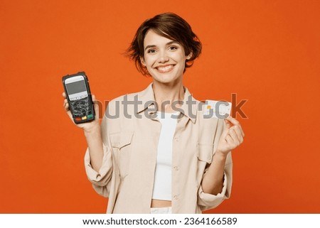 Young happy caucasian woman she wears beige shirt casual clothes hold wireless modern bank payment terminal to process acquire credit card isolated on plain orange red background. Lifestyle concept