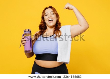 Young chubby overweight plus size big fat fit woman wear blue top warm up train hold towel bottle drink water do winner gesture isolated on plain yellow background studio gym. Workout sport concept