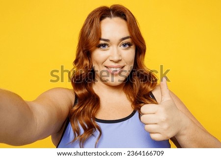 Close up young chubby overweight plus size fat fit woman wear blue top warm up train do selfie shot pov on mobile cell phone isolated on plain yellow background studio home gym. Workout sport concept