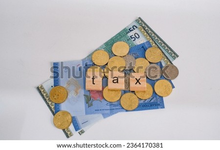 The word "tax" on wooden block sitting on top of a pile of money. Financial and economy concept