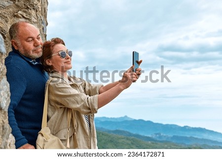 Middle aged traveler couple have fun in mountain using smartphone to take selfie. Mental health, wellbeing, trip adventure and healthy lifestyle.