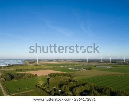 Aerial drone shot of wind turbine power generators lining the A16 highway in the Netherlands with edge of Hollands Diep river on sunny summer day. Traffic flows across the wide stretch of fresh water 