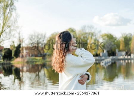 Young beautiful dark haired woman in knitted cardigan near the lake. Cozy autumn. Warm spring. Fall.