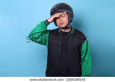 Exhausted young Asian online driver man wearing helmet touching head showing tired expression Royalty-Free Stock Photo #2364188145