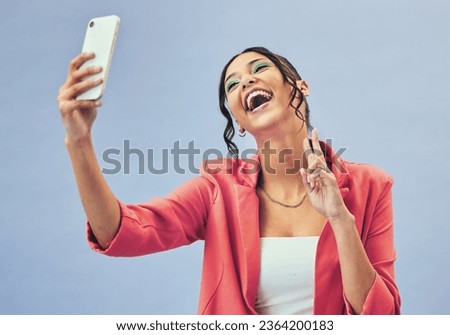 Phone, laugh selfie and woman with a peace sign from social media and picture for creative job in studio. Influencer, happy and makeup with career fashion with blue background and emoji hand sign