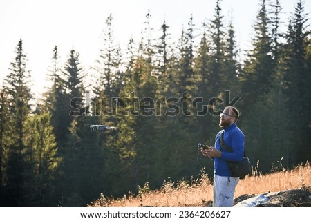 Professional photographer taking photos from drone. Young man taking aerial photos in mountains. Man controlling his drone on background of mountain forest.