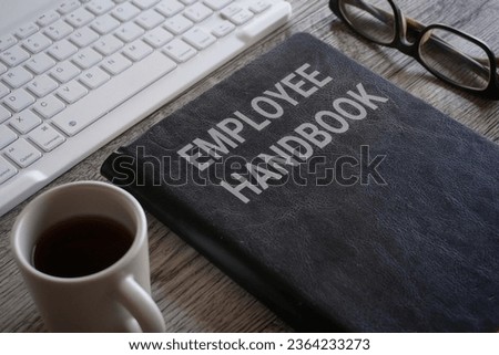 Closeup image of book with text EMPLOYEE HANDBOOK surrounded by cup of coffee and glasses on office desk Royalty-Free Stock Photo #2364233273