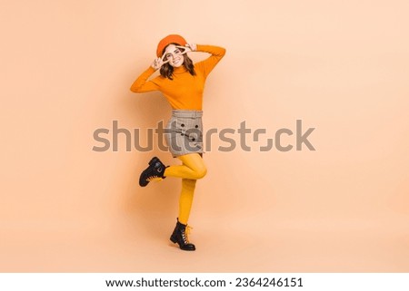 Full length photo of cheerful carefree lady wear trendy orange outfit arms showing v-sign empty space isolated on beige color background