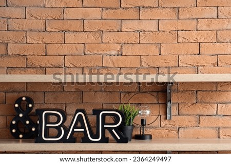 Shelving unit with decorative sign BAR hanging on brown brick wall