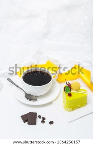 Cup of coffee with heart-shaped cake in yellow glaze on a plate on a table on a white background