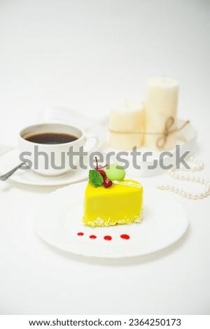 Cup of coffee with heart-shaped cake in yellow glaze on a plate on a table on a white background
