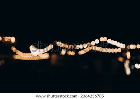 Decorative string lights at night time, Defocused Background, night city life backdrop, party time with Yellow bokeh balls. Warm festive bokeh of string lights over an outdoor bar or patio at twilight