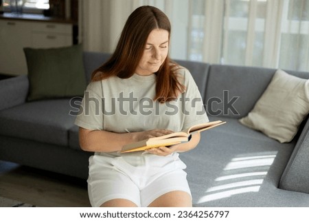 Brunette female with book sitting on textile couch. Happy beautiful woman reading book at home. Concepts of education and comfort. High quality photo