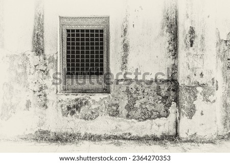 A flitered monochrome image of a carved window opening with bars on the exterior of a traditional Arabian house with weathered walls. Royalty-Free Stock Photo #2364270353