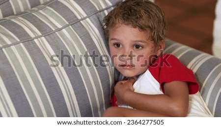 Young boy toddler watching TV at home lying on sofa. Child watches content on couch in the evening