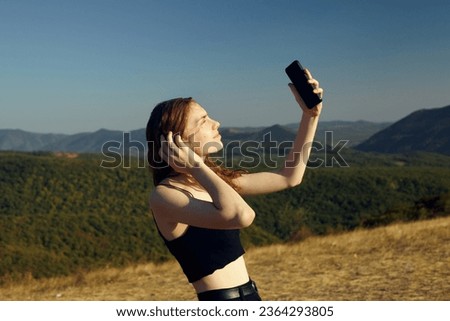 a woman on the background of mountains with a phone in her hands, takes a selfie on a sunny clear day