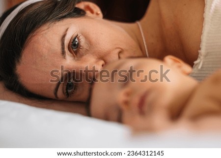 Mom with tired face and lost look, next to her baby as she sleep Royalty-Free Stock Photo #2364312145
