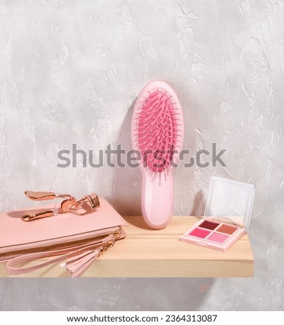 A pink hairbrush, eye shadow for beautiful fashionable makeup, a woman's pink wallet for money or business cards.
