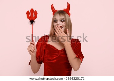 Surprised young woman dressed for Halloween as devil on pink background