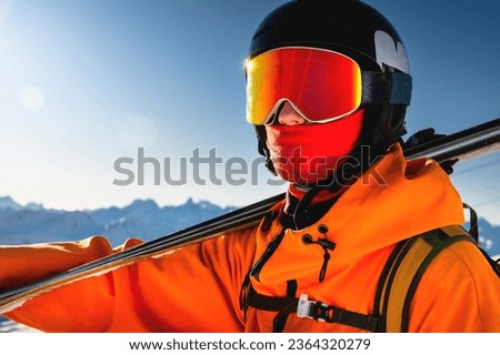 Portrait of a skier with skis on his shoulder. Guy on a background of a mountain range on a sunny winter day, sunlight, outdoor recreation, skiing, sports concept