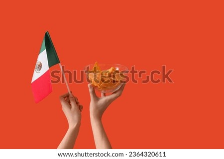 Female hands holding mexican flag and nachos on orange background