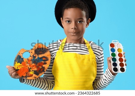 Little African-American boy with paints and palette on blue background