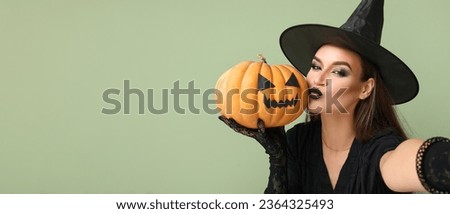 Young woman dressed for Halloween as witch with pumpkin taking selfie on green background with space for text