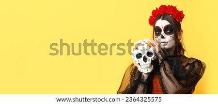 Young woman holding painted skull on yellow background with space for text. Celebration of El Dia de Muertos (Mexican Day of the Dead) Royalty-Free Stock Photo #2364325575