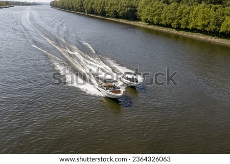 Two small boats sailing at high speed on calm waters along Albert canal, lush green trees, blurry and foggy background, sunny summer day in Liege province, Belgium Royalty-Free Stock Photo #2364326063