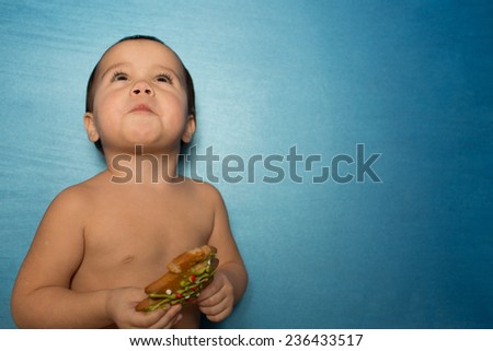 portrait of young infant adorable baby girl sitting on blue background and eating cookie