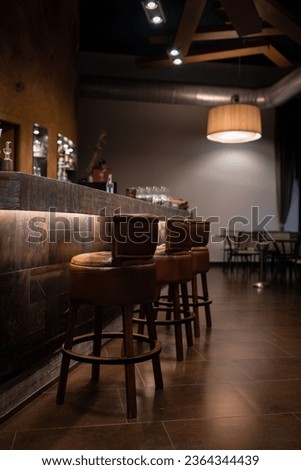 Several leather-covered bar stools are arranged in a row along a bar counter Royalty-Free Stock Photo #2364344439