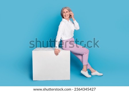 Full length profile photo of positive aged lady sit podium look empty space ad isolated on blue color background