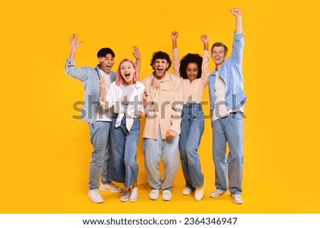 Winner concept. Group of diverse teen friends clenching fists, standing together over yellow background, excited for success with arms raised, celebrating victory Royalty-Free Stock Photo #2364346947