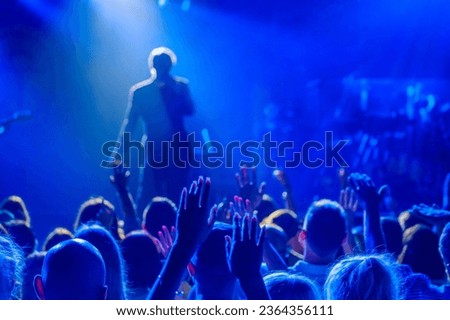 Back view of crowd of unrecognizable people dancing with raised arms while standing near stage during concert of male singer and musician in club Royalty-Free Stock Photo #2364356111