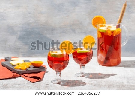 Front view of freshly prepared beautiful red coloured sangria served in glass pitcher on white vintage table, garnished with apples and oranges and in two glasses filled with ice Royalty-Free Stock Photo #2364356277