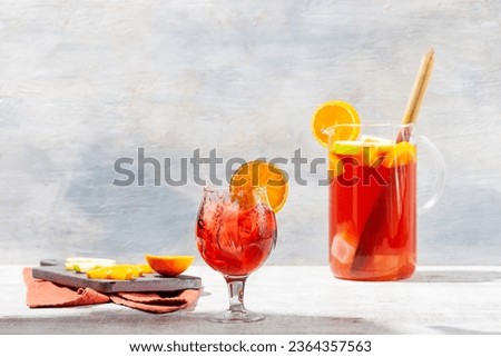 Freshly prepared beautiful red coloured sangria served in a glass pitcher on white vintage table, garnished with apples and oranges and with splash effect in glass filled with ice Royalty-Free Stock Photo #2364357563