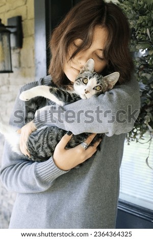 Young woman holding a grey and white tabby adolescent cat she adopted from the animal shelter. Selective focus with blurred background.