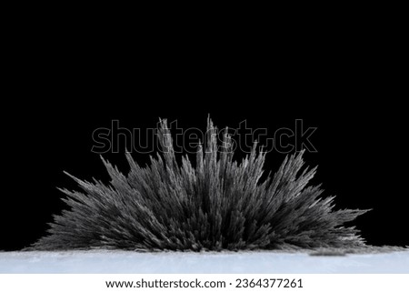 A reaction of iron dust to a magnetic field of a strong neodymium magnet on a black background Royalty-Free Stock Photo #2364377261