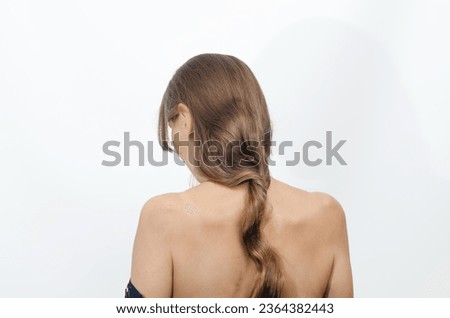 Woman stands with her back to the camera, hair tied up in a cord