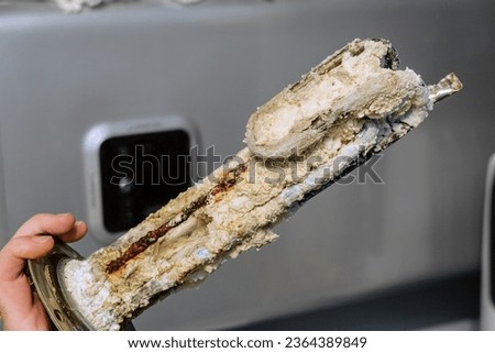 Heating element of an electric water heater with a rusty anode and a tube covered with scale. Serviceman holds a damaged part in his hand. Service and repair. Royalty-Free Stock Photo #2364389849