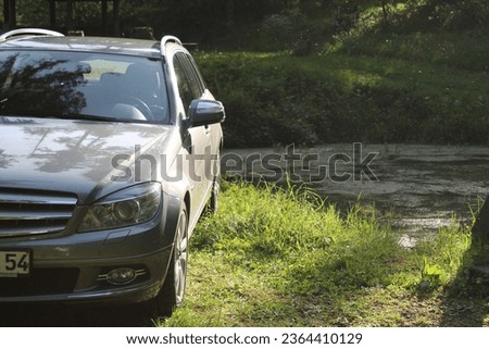 The car parked on the green lawn against the background of the river. Royalty-Free Stock Photo #2364410129