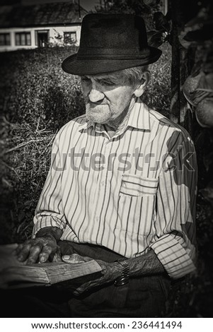 Portrait of an expressive old farmer reading leaning on an apple tree. Close-up portrait. Black and white picture.