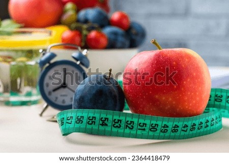 Nutrition, weight loss, water balance, daily routine control. Tape measure for measuring the size around an apple, a clock and a lot of vegetables and fruits in the background, horizontal.