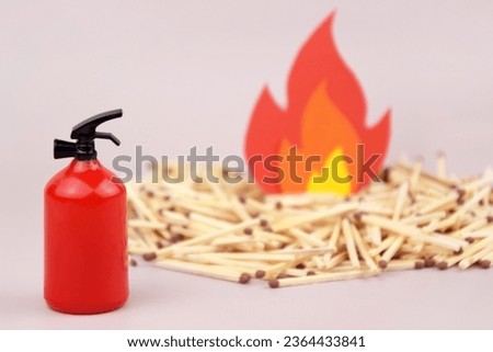 A box of matches placed next to a toy red fire extinguisher against a light background. Fire safety concept. International Firefighter's Day.
