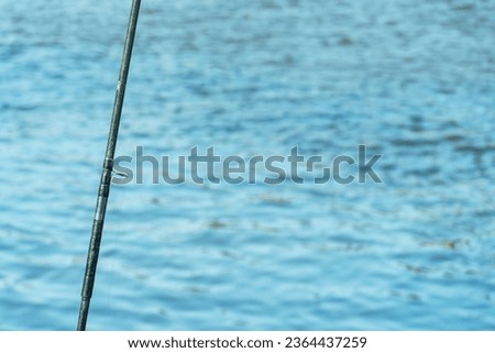 Modern carbon fishing rod close-up on the background of the lake. Fishing gear and lures for fishing in difficult conditions.