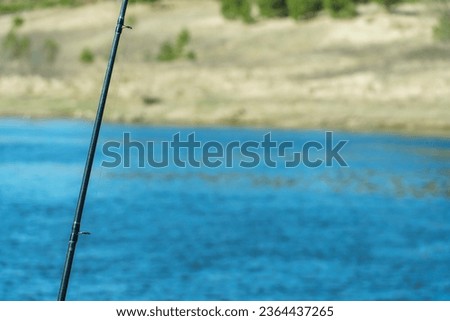 Modern carbon fishing rod close-up on the background of the lake. Fishing gear and lures for fishing in difficult conditions.