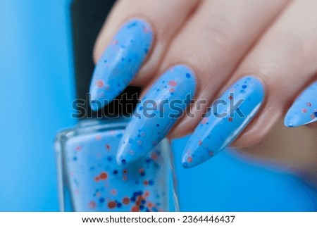 Woman's beautiful hand with long nails and light blue manicure with bottles of nail polish