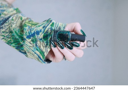 Woman's hand with long nails and dark green nail polish